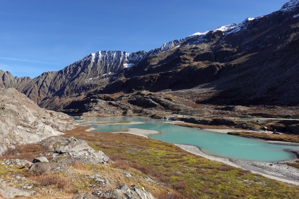 Türkiser, ungeregelmässig geformter Bergsee mit Vegetation um den See, steile Wände im Hintergrund.